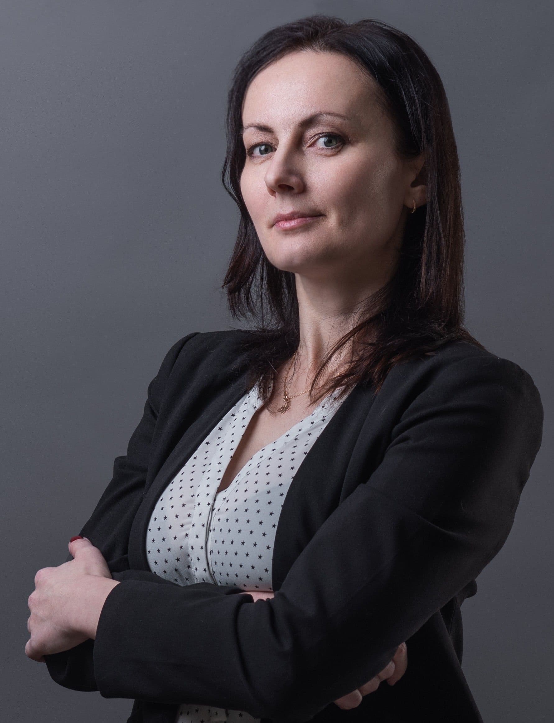 Confident woman with dark hair and a black blazer, arms crossed, looking at the camera.